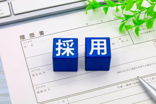 履歴書の用紙の上に置かれた「採用」の文字のブロックとペン