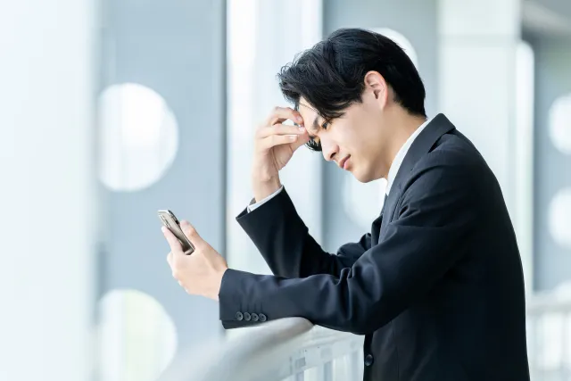 スマートフォンを見ながら考え込むスーツ姿の男性